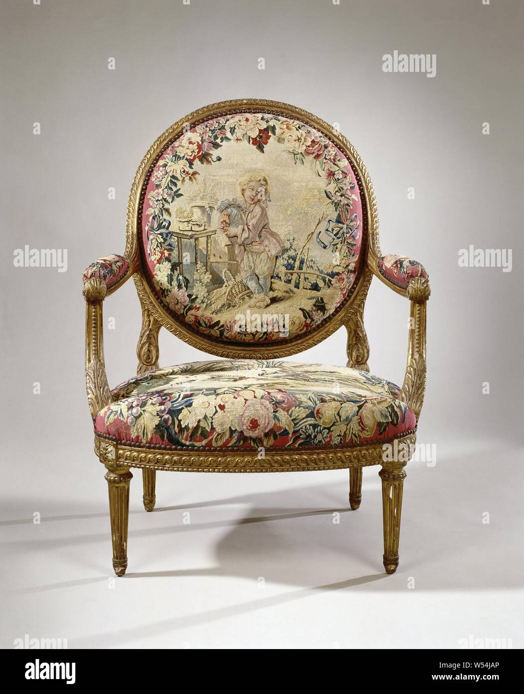 Armchair upholstered in tapestry with a boy playing on a bagpipe (petit joueur de cornemuse) (back) and a dog hunting ducks (seat), Armchair of gilded beech wood, resting on conically shaped legs. The armchair belongs to an ameublement. On the pink curved seat frame and the covered oval back window, on a pink fond, representations are made within flower wreaths (tapestry de Beauvais)., Manufacture Royale des Gobelins, France, c. 1755 - c. 1765 and/or c. 1935, walnut (hardwood), gilding (material), ketting, inslag, gilding, h 101 cm × w 78 cm × d 75 cm h 43 cm × d 53 cm Stock Photo