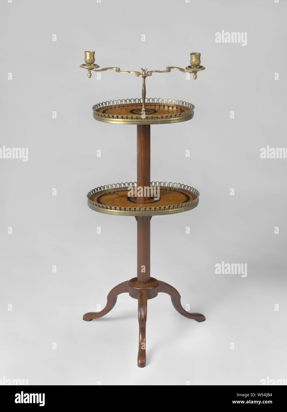 Table, decorated with marquetry and standing on three broken S-shaped, radially placed feet, with cylindrical crossroads and trunk decorated with grooves. With two oval sheets with gilt bronze edging, Table decorated with marquetry of satin, rosewood and ebony on an oak core. Three broken S-shaped feet placed radially on a cylindrical intersection carry the round trunk, adorned with grooves. At oval height and on top are oval sheets that have marquetry edges with circular protuberances and have a gilt bronze border with a gallery around them. In the middle of the trunk an adjustable steel bar Stock Photo