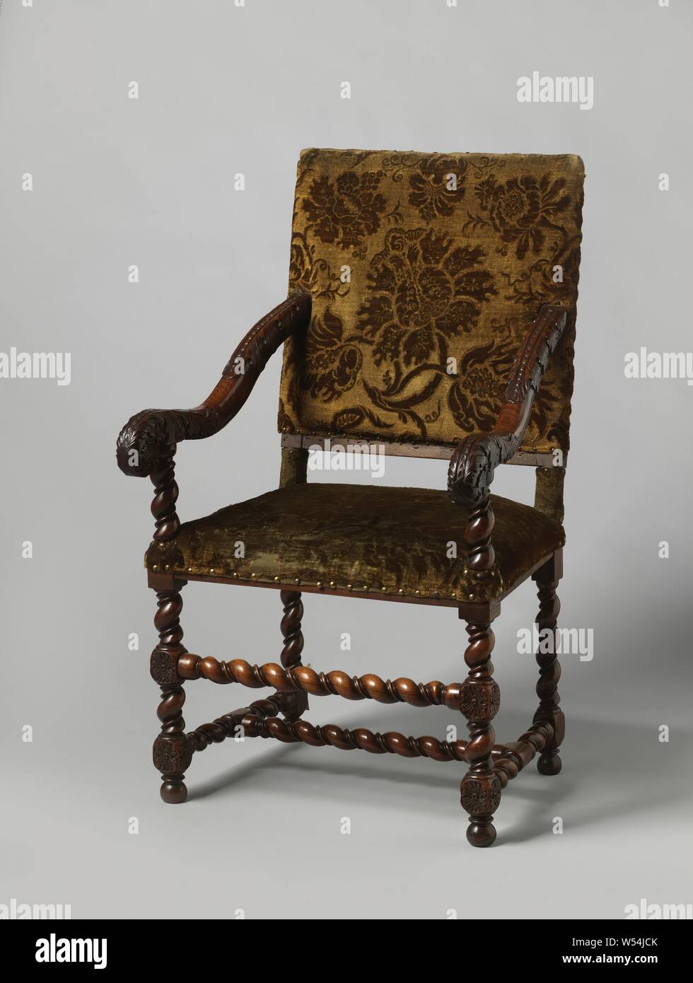 Armchair with slung legs, upholstered in bronze-colored floral trim, Armchair in walnut, upholstered in bronze-colored floral trim. The furniture rests on slung legs that are connected by an equally slung H-shaped cross and front-center sport, a bead has been placed between the pendulum. The houses have stabbed rosettes. The armrest struts are concave, run up in the back window and end in volutes, which, like the back, are adorned with acanthus leaves with scaly middle veins., anonymous, Northern Netherlands, 1675 - 1700, wood (plant material), walnut (hardwood), h 113.5 cm × w 67 cm × d 68 cm Stock Photo