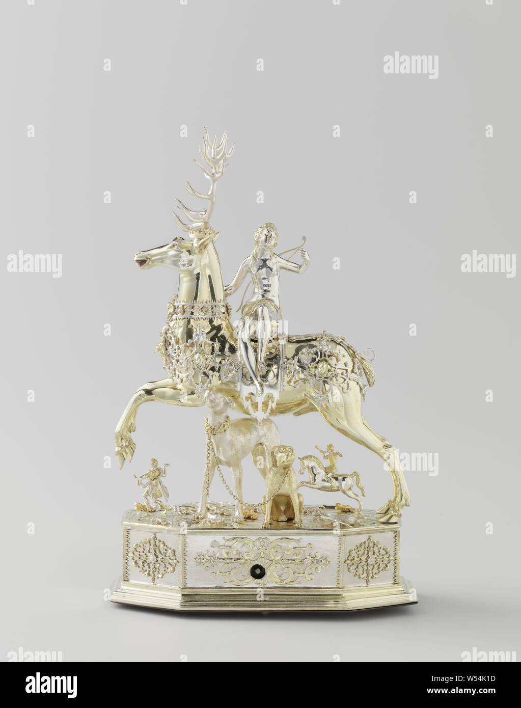 Table automaton in the form of Diana on a stag, Table automaton in the form of Diana on a deer, Diana, seated on a deer. Automatic silver, partly gold-plated. The deer, which has a removable head and wears a crown, is surrounded by openwork band ornament. Similar decorations around the eight-sided pedestal, on which all kinds of insects and animals are placed on a natural base, including two hunting dogs, a horseman and a hunter. A few holes point to other lost additions. Diana looks back. She wears a bow and an arrow quiver on the back and holds in her raised left hand the end of the chain Stock Photo