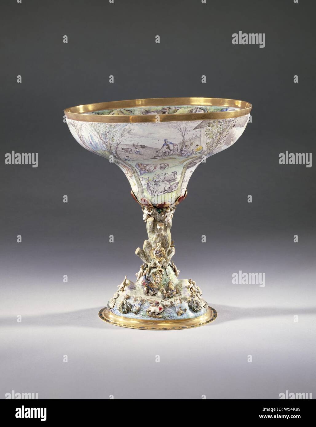 Cup Cup with representations from the Metamorphoses of Ovid, Cup of gold, completely enameled on a white background. The base of the cup, with a flat ring with diamond pattern, is shaped like a hill with a gnarled tree trunk at the top, which serves as the trunk of the cup. Enameled gold figures are attached to the foot completely covered with enamel. Orpheus sits against the tree trunk, playing on his viola. At his feet are amors, mermaids and many birds, including a peacock, a rooster, a parrot, two swans and two eagles. The top of the tree trunk is surrounded by amors and red enameled Stock Photo