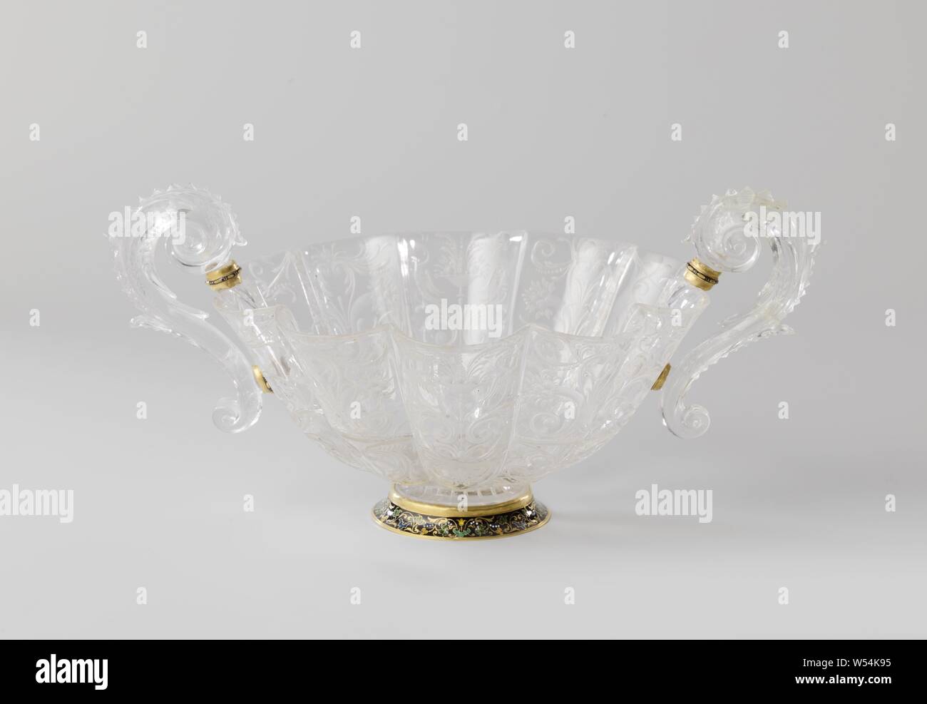 Footed dish Dish, ten-lobed, of rock crystal with a black enameled base of gold. Dish decorated with tendrils, fruit bunches and birds in grinding work. Two S-shaped ears of crystal, Tienlobige, deep bowl of rock crystal with a black enameled golden base. The bowl is decorated with tendrils, fruit bunches and birds in grinding work. Two S-shaped crystal ears., Ornaments, art, anonymous, Milaan, c. 1550 and/or c. 1650, gold (metal), h 14.5 cm × w 30.7 cm × d 21.6 cm Stock Photo