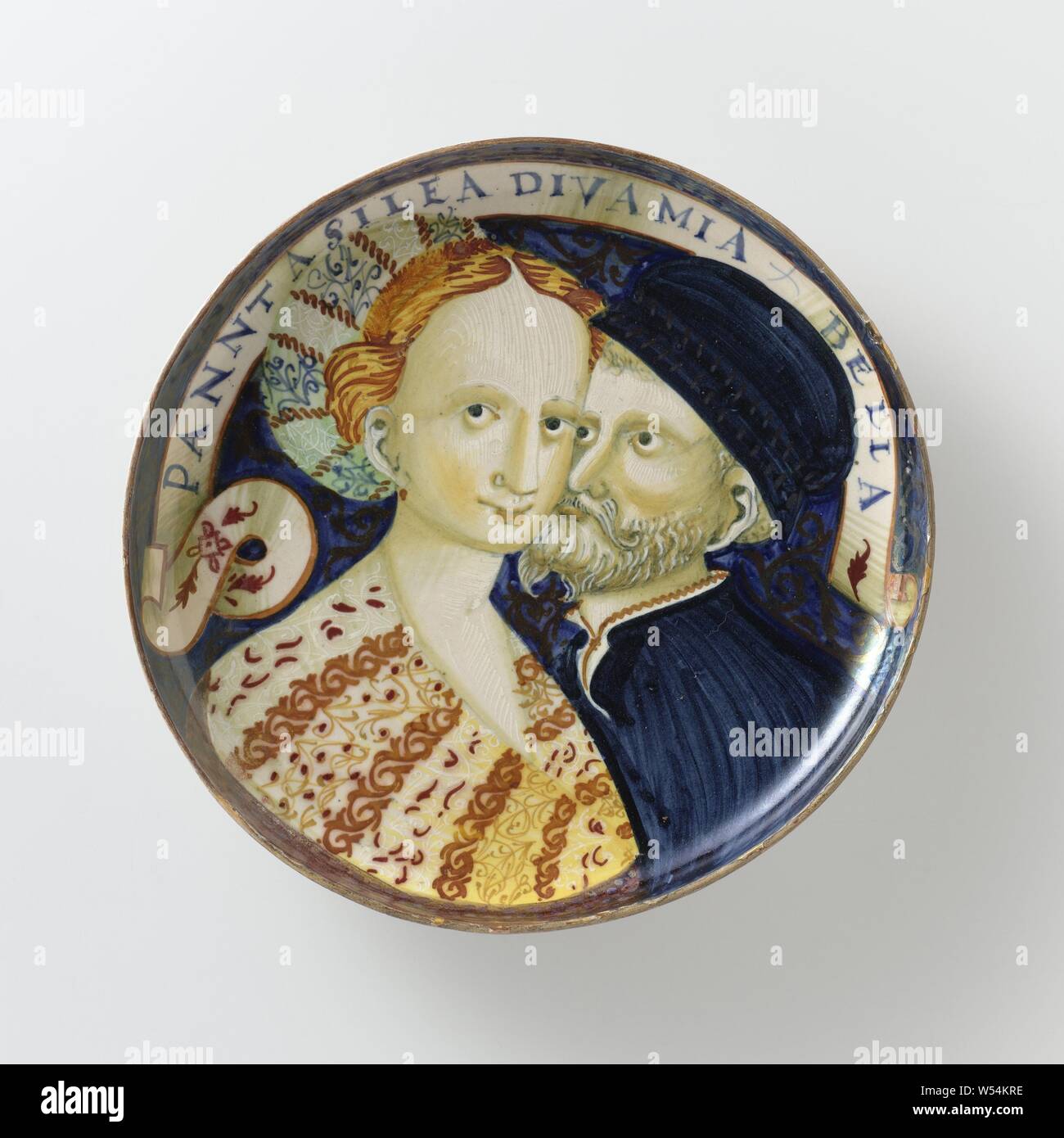 Dish with a man and a woman, Dish on foot with portrait of a man and a woman with the inscription: PANNTASILEA DIVA MIA BELLA, Dish on foot of multi-colored majolica. Painted on blue ground with the busts of a young woman and a bearded man. Both are wearing hats. The women's clothing is richly decorated. Along the upper edge runs a banderolle with the inscription 'PANNTASILEA DIVA MIA BELLA' (Penthesileia, my divine beauty). The bowl is provided with extra decoration in metal luster in gold and red, couple or lovers, anonymous, c. 1530 - c. 1540, earthenware, tin glaze, lead glaze, luster Stock Photo