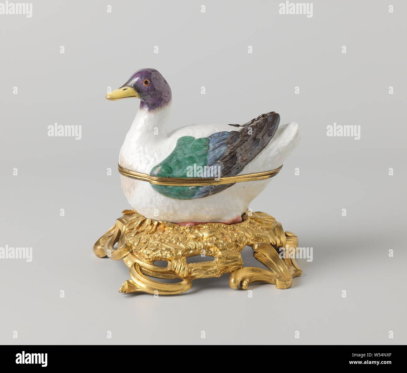 Box with lid in the shape of a duck on a pedestal, Box of painted porcelain. The box has the shape of a duck. The duck sits on a gilt bronze rococo pedestal. The duck is partly painted in blue, green, brown-gray and black, the head in blue, purple and gray with a yellow beak. The box is unnoticed., Meissener Porzellan Manufaktur, Meissen, c. 1740 - c. 1748 and/or c. 1750, porcelain (material), bronze (metal), gilding, h 5.5 cm w 16.7 cm × d 19 cm h 5.2 cm w 9.5 cm × d 14.5 cm h 9 cm w 9 cm × d 17.5 cm h 18.5 cm Stock Photo
