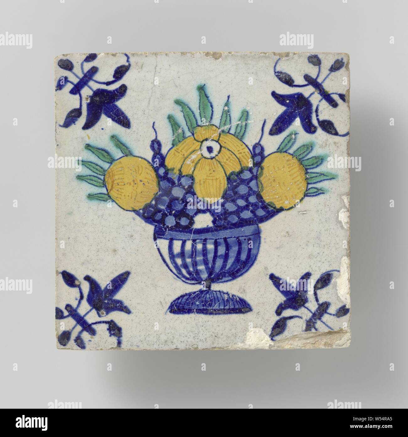 Tile with fruit basket, Tile with a multicolored (blue, green, orange and yellow) fruit basket. In the corners, a lily., anonymous, Netherlands, c. 1640 - c. 1660, earthenware, tin glaze, h 13 cm × w 13 cm × t 1.5 cm Stock Photo