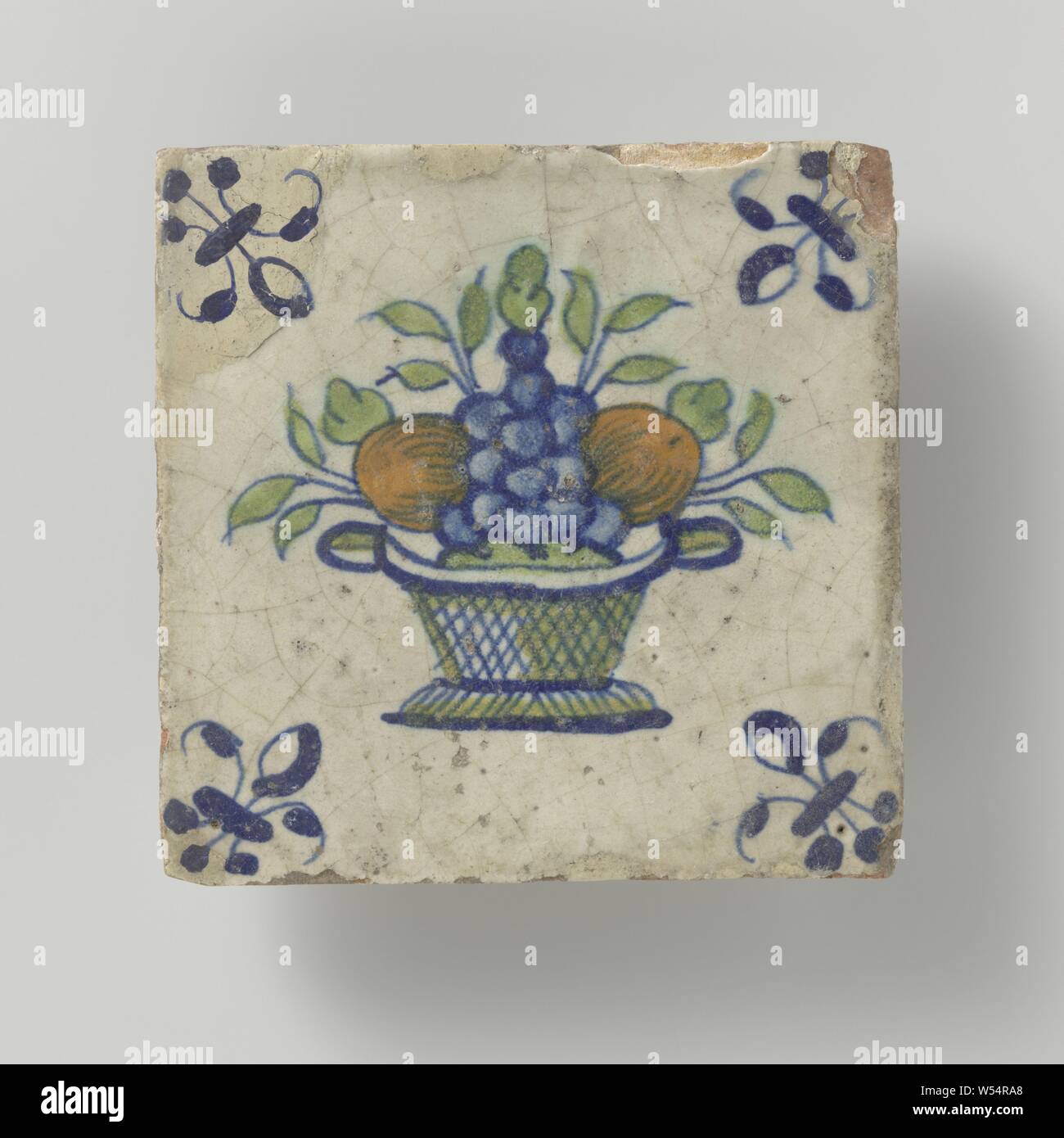 Tile with fruit basket, Tile with a multicolored (blue, green and orange) fruit basket with a lily in the corners., anonymous, Netherlands, c. 1640 - c. 1670, earthenware, tin glaze, h 12.8 cm × w 12.8 cm × t 1.5 cm Stock Photo