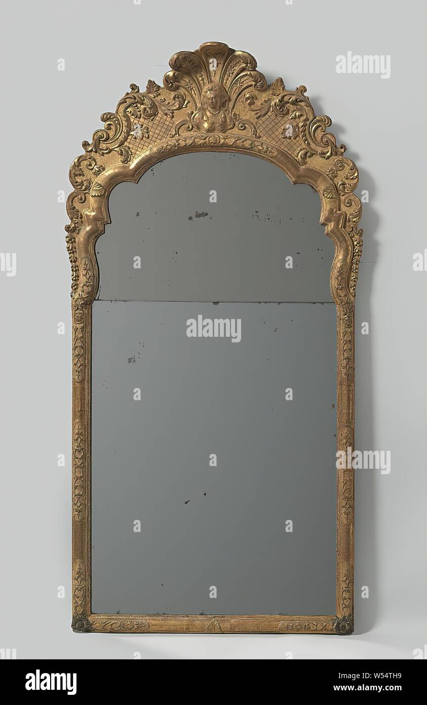 Mirror with frame of gilded lime wood, sculpted with S- and C-volutes, interrupted bandwork, rosettes, palmettes and with a woman's bust on the top center, Mirror enclosed in a frame of gilded and sculpted lime wood. The scalloped upper sill has an attachment with a woman's bust placed in the middle for a palmetal motif. On both sides, symmetrical C and broken S leaf leaves are applied to partially checkered soil. The frame is decorated with an interrupted bandwork motif, on the corners and in the transition to the upper threshold with rosettes in the middle, and with some palmettes. Stock Photo