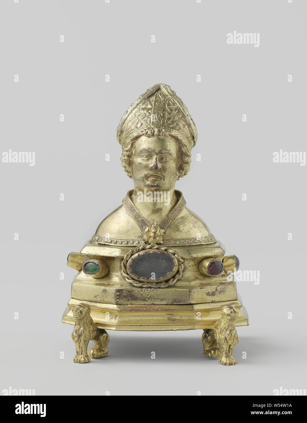 Reliquary Reliquary holder in the form of a bust of a bishop, The object consists of the following cast and hammered main parts: the bust with the pedestal, the base under the pedestal and the four lions. The bust represents a bishop, a middle-aged man, with a shaved face, curly hair reaching down to the neck, and a few strands that rise above the forehead just below the miter. The miter, which is covered from above, is adorned with bands that are arranged both along the edges and across the centers towards the miter points. They feature engraved tendrils ornament or trimmed with cast sheet Stock Photo