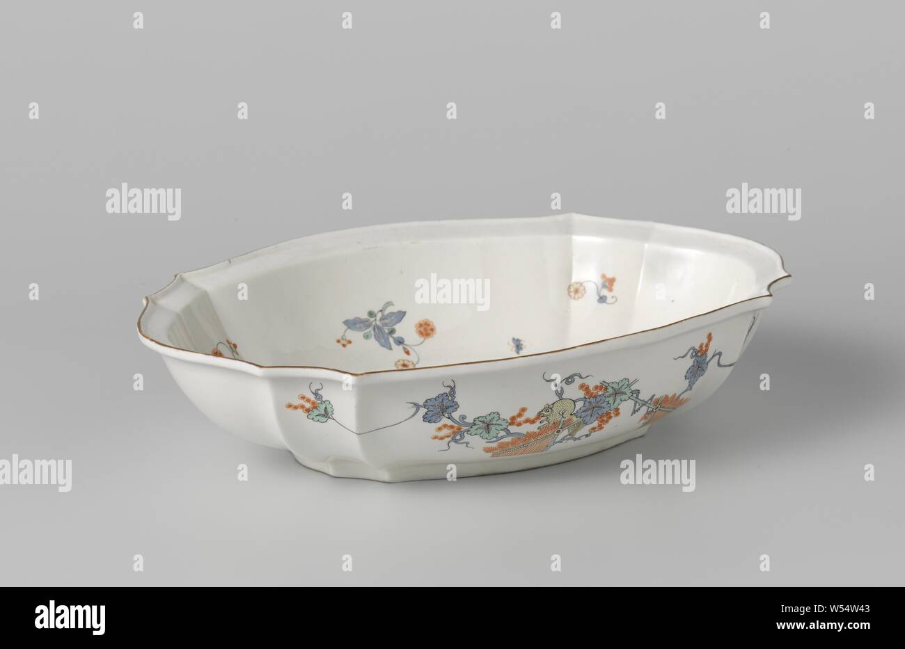 Bowl with a squirrel and flowering plants near a rock, Scalloped, oval bowl of soft-paste porcelain (pâte tendre), painted on the glaze in blue, red, green, yellow and black. Flowering plants (chrysanthemum) on the outside wall behind a bamboo fence near a rock and on the other side a squirrel on vines near a fence. A butterfly on the narrow sides. One large and smaller flower spheres with butterflies on the inside. Brown border. Marked on the bottom with the handset. The jug is in the style of the Japanese Kakiemon porcelain., Chantilly, c. 1740, porcelain (material), soft-paste porcelain Stock Photo
