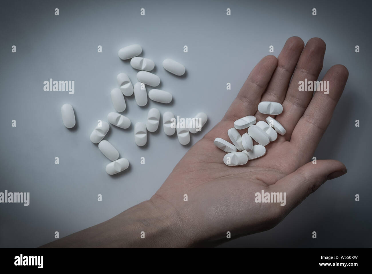 Hand holding many white prescription drugs, medicine tablets or vitamin pills in a pile - Concept of healthcare, opioids addiction, medicament abuse Stock Photo