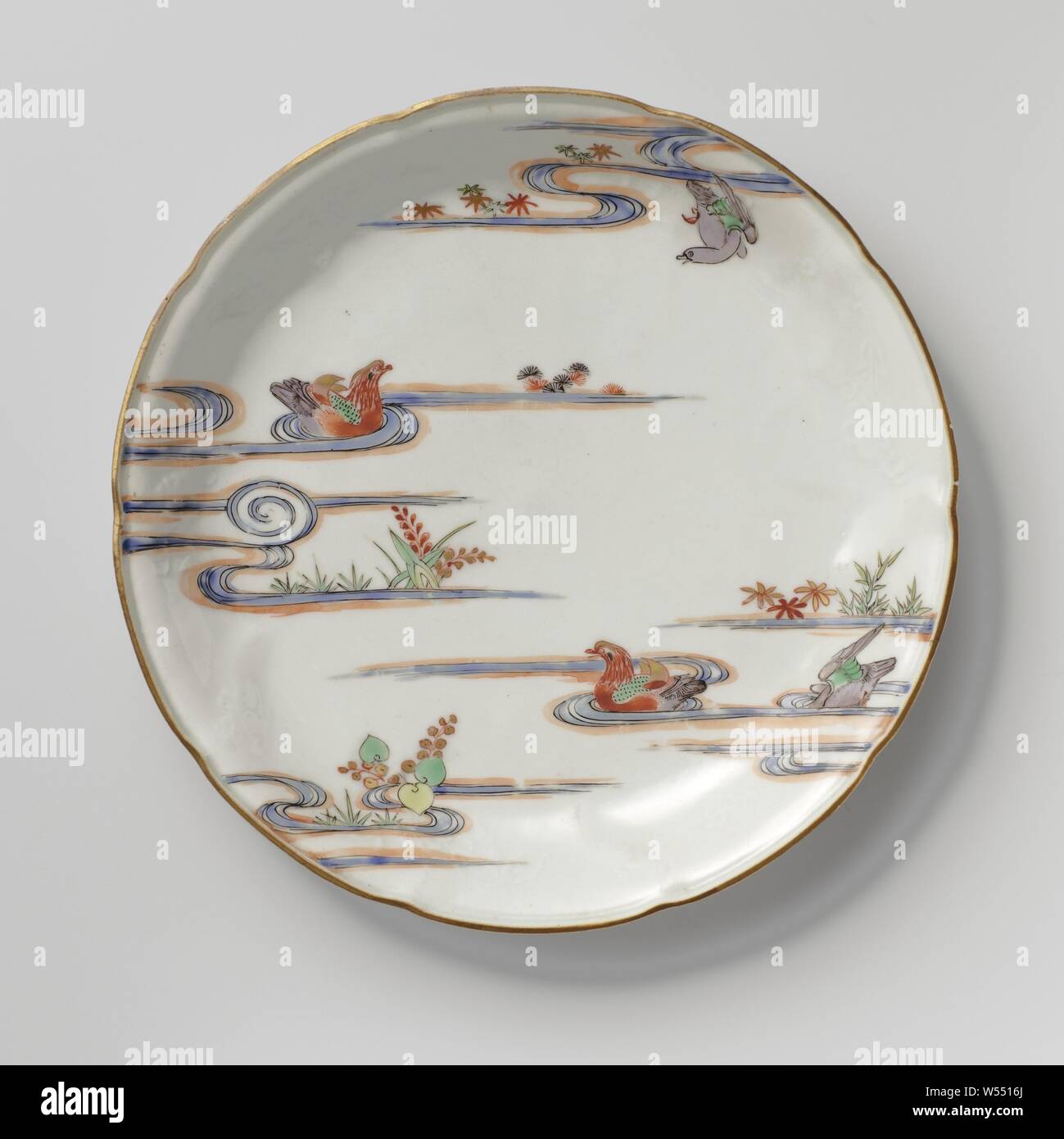 Saucer-dish with flower sprays in relief and two mandarin ducks in a pound, Porcelain dish with a scalloped edge, painted on the glaze in blue, red, green, yellow, eggplant, black and gold. On the front on the wall, flower branches in relief, two tangerine ducks in enamel colors in a pond with plants and a flying bird. The outside with flowering water plants. Five proen on the bottom. Kakiemon style., anonymous, Japan, c. 1675 - c. 1724, Edo-period (1600-1868), porcelain (material), glaze, gold (metal), vitrification, h 3.1 cm d 21.7 cm d 13.8 cm Stock Photo