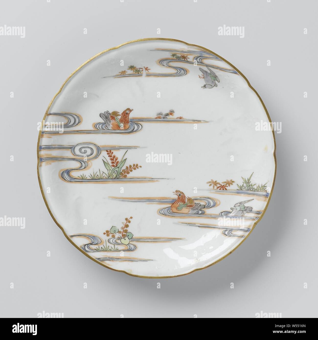 Saucer-dish with flower sprays in relief and two mandarin ducks in a pound, Porcelain dish with a scalloped edge, painted on the glaze in blue, red, green, yellow, eggplant, black and gold. On the front on the wall, flower branches in relief, two tangerine ducks in enamel colors in a pond with plants and a flying bird. The outside with flowering water plants. Five proen on the bottom. Kakiemon style., anonymous, Japan, c. 1675 - c. 1724, Edo-period (1600-1868), porcelain (material), glaze, gold (metal), vitrification, h 3.1 cm d 21.7 cm d 13.8 cm Stock Photo