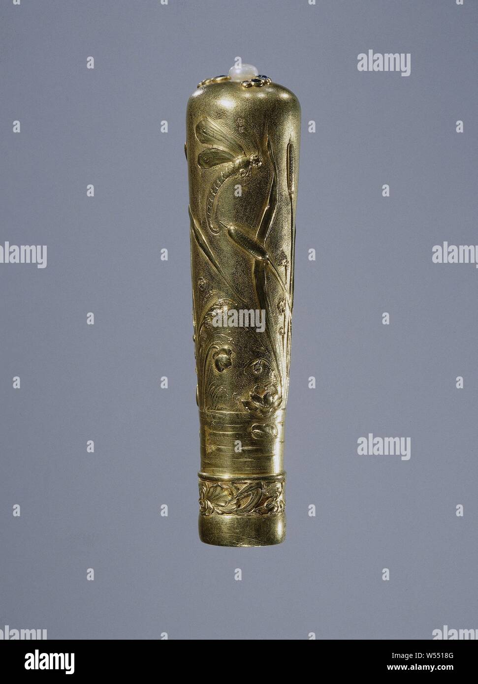 Parasol bud of gold, decorated with water lilies, cattail and dragonfly, Parasol bud of gold. The button is oval from below and extends to the round, slightly convex top. It rests on a slightly curved, smooth belt, above which is driven a frieze of a repeating pattern of lily-like flowers against a roughened background. The upper side is decorated with a pearl, from which three C-shaped garlands run, each of which consists of four decreasing golden settings with alternating sapphires and diamonds. The bud is driven all around with water and various plants such as water lilies, cattail and reed Stock Photo