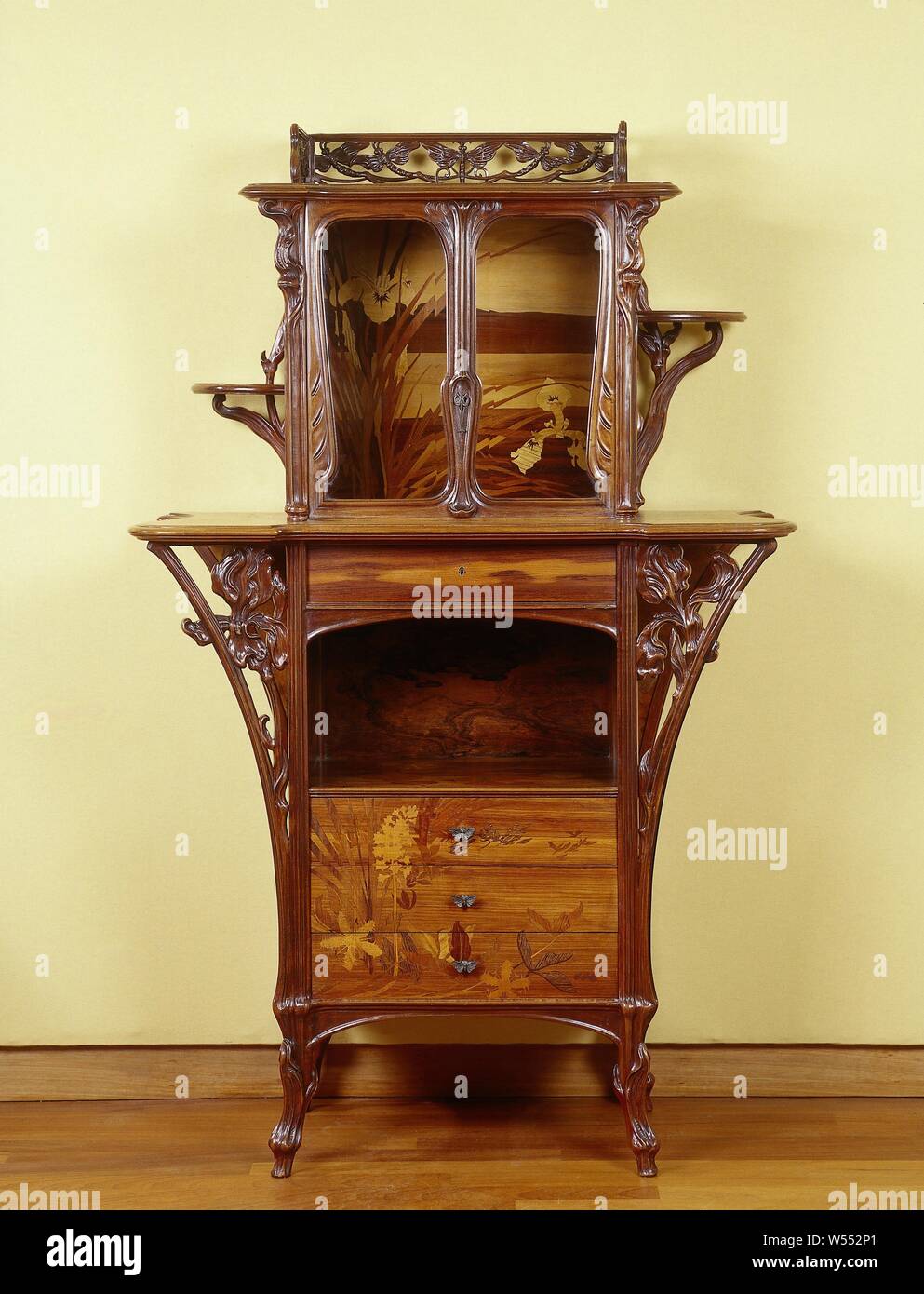Display case with marquetry in floral motifs, Display case made of oak and fruit wood, glued with elm roots, rosewood and maple wood resting on four high legs. The cupboard consists of a lower and upper cupboard that are separated from each other by means of a top that protrudes on both sides. The base unit consists of an open block with three drawers at the bottom, an open part in the middle and a drawer at the top. The three drawers contain marquetry in the form of irises and water triple and have tractors of gilt bronze in the form of butterflies. The top drawer has a keyhole in the middle Stock Photo
