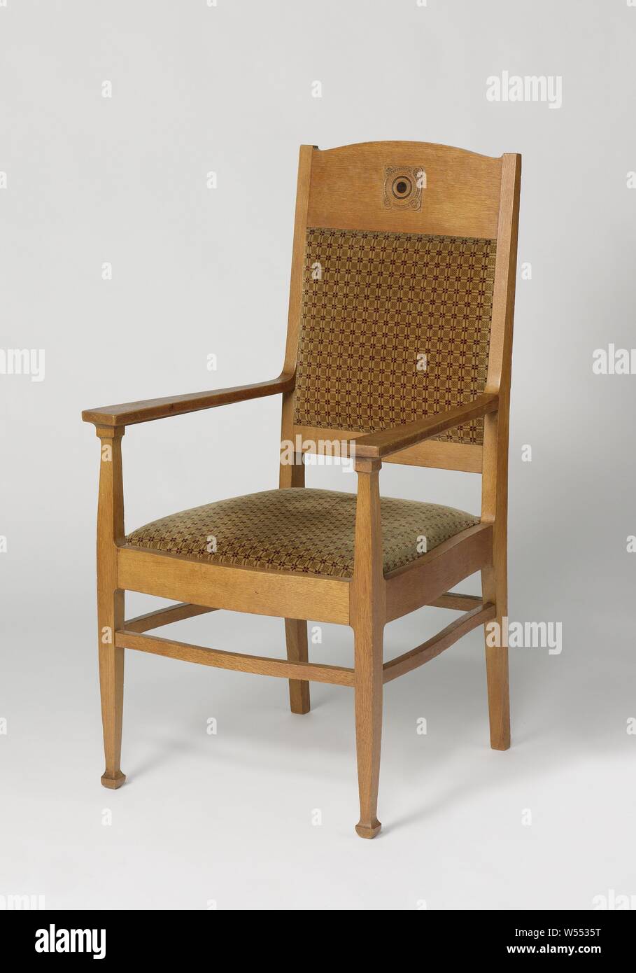 Armchair with a carved braided rosette and covered with green stripe with red diamond patterns, Armchair of oak resting on four curved legs. The legs are interconnected by means of curved lines. The front legs continue in the struts for the armrests. The hind legs continue in the back posts. The backrest consists of a panel with a rounded top on the top and a line on the bottom. The open space in between is covered with green cloth with red diamond motifs. On the panel at the top is a carved braided rosette with pearl edges and inlaid with ebony in the middle. The armrests widen to the front Stock Photo