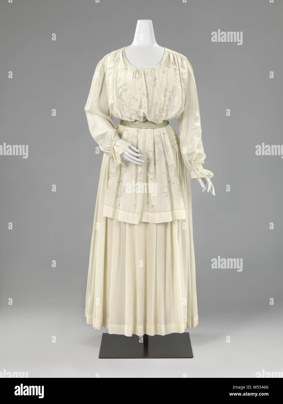 Frock with lap blouse, Frock of cream-white crêpe de chine with a wide skirt with smocking on the hips and a blouse with loose, tunic-like buildings with embroidery in white and light green silk, 'and Canadian'. Model: Ankle-length, with a pleated skirt at the waist. Low round neck (probably twisted and entertained in the past?) And loose-fitting long sleeves with pleated cuffs that fall over the hand. Blouse in body, wrinkled steps on the shoulders and open seams in the side seams. Front and rear loose-hanging building, which should give the impression of a tunic. Belt made of soft green Stock Photo