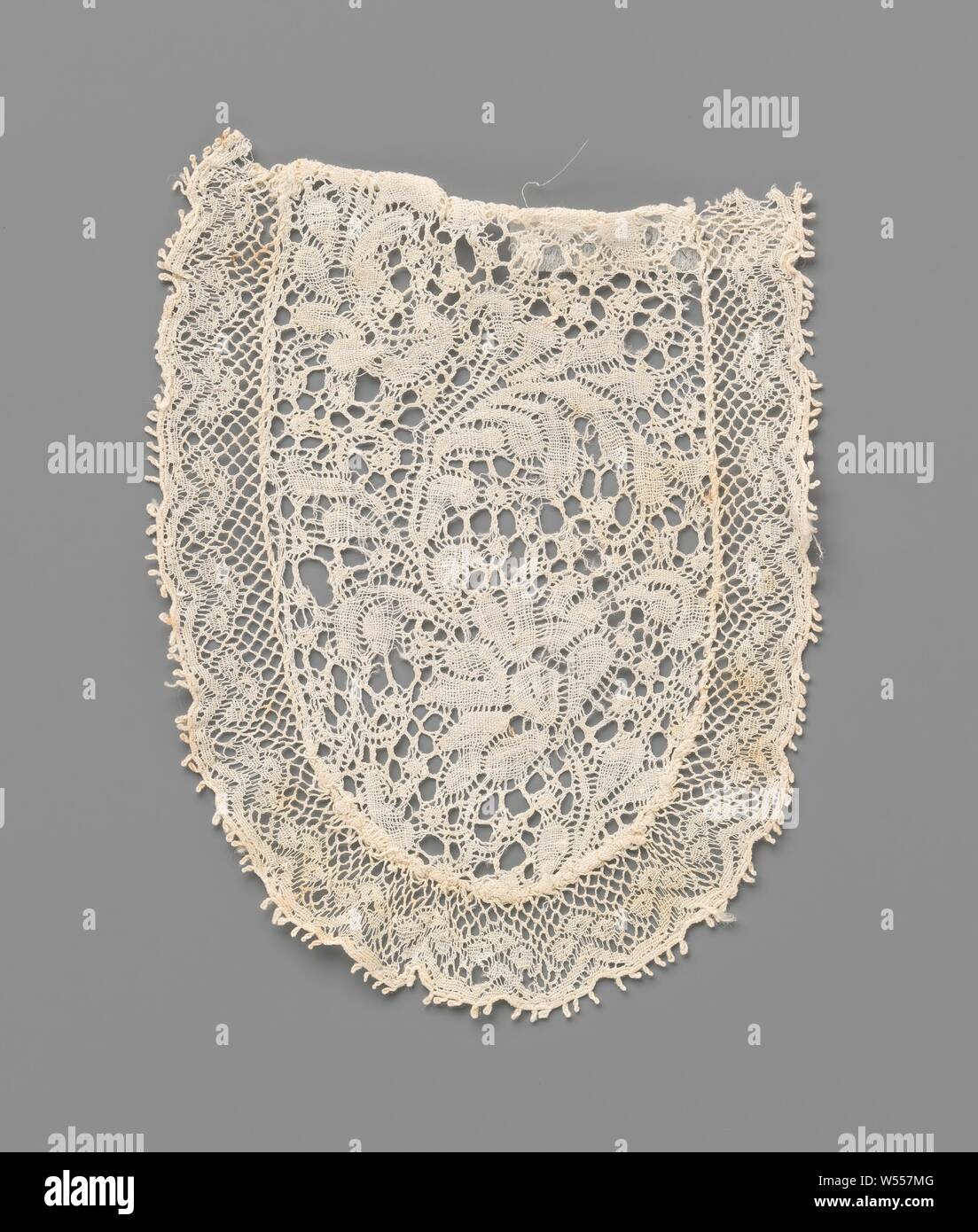 Bobbin lace jabot with a wave of a fan-shaped flower and feathered leaves, A small jabot of natural-colored bobbin lace, Binche lace with a Valenciennes lace edge. The model is rectangular with one rounded short side, like a half oval. The Binche lace pattern consists of a curved flower stem, with a fan-shaped flower, from which a large feathered leaf rises that deflects in the opposite direction. The motifs are connected by a decorative ground, a snow ground. The motifs are made in linen with openwork edges. The straight short side is finished with a hem. The other sides are finished Stock Photo