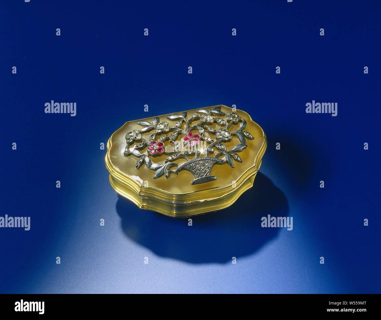 Gold snuff box with chalcedony lid. The scalloped box is decorated with a flower basket in relief of silver, with diamonds and rubies. The scalloped gold box, with a straight back, has a hinged lid. The wall of the box is articulated by a profile edge, below it is slightly convex, rejuvenating itself to the flat bottom, above it is slightly strapped. On the convex part it is engraved on the front with a flower basket. the lid is made of chalcedony, mounted in a raised tab. It has an imposed decoration of a cast silver flower basket, with horrified and engraved details, set with diamonds Stock Photo