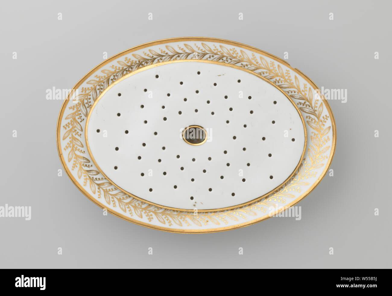 Dish with the coat of arms of Hendrik Peter Godfried Quack and Isabella Gertraud von Carnap, Oval dish (fish dish) with porcelain drip plate, painted on the glaze with gold. On the flat the alliance weapon of Hendrik Peter Godfried Quack and Isabella Gertraud von Carnap. The border with a flower tendril and a gold band. Double foot ring. The drip plate has a golden edge and has a large hole in the center with small holes around it. Marked on the bottom with B.L., E. Blancheron, c. 1790 - c. 1800, porcelain (material), glaze, gold (metal), vitrification Stock Photo