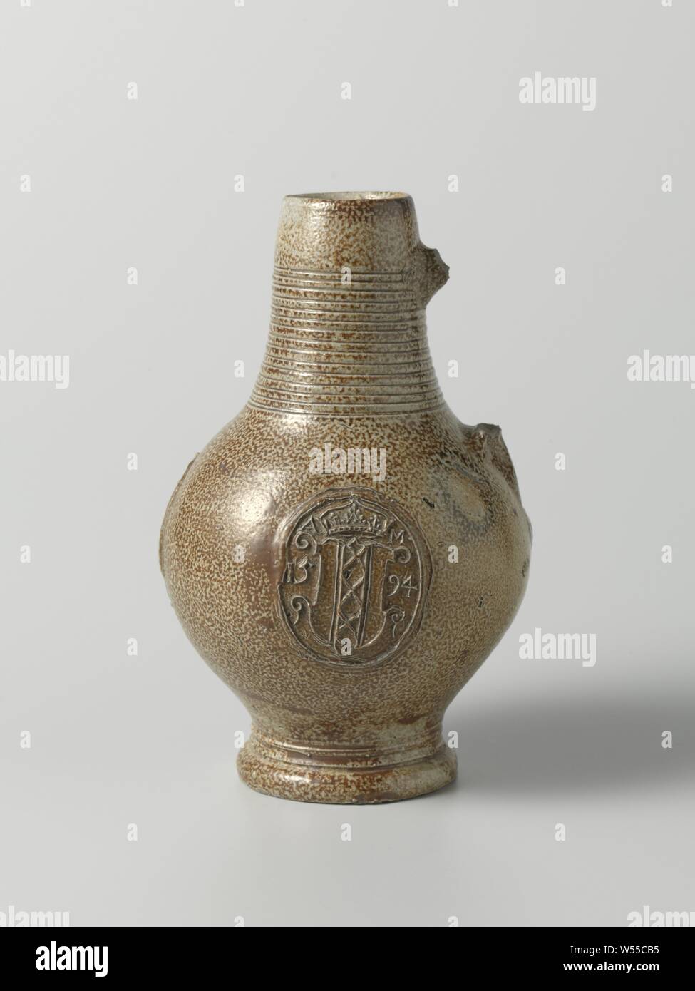 Jug with the coat of arms of Amsterdam, Jug of stoneware on high feet with a spherical body and a tapered neck. The C-shaped ear (missing) is attached to the neck and shoulder. A wide band with incised lines on the neck, profiles on the foot. Covered with a brown engobe. On the belly three times a printed and imposed medallion with the crowned weapon of Amsterdam in relief. On the weapon the inscription 'AM' and the date '1594'. Raeren., anonymous, Raeren, c. 1594 - c. 1610, stoneware, glaze, engobe, vitrification, h 18.8 cm d 4.3 cm d 11.7 cm d 7.2 cm Stock Photo