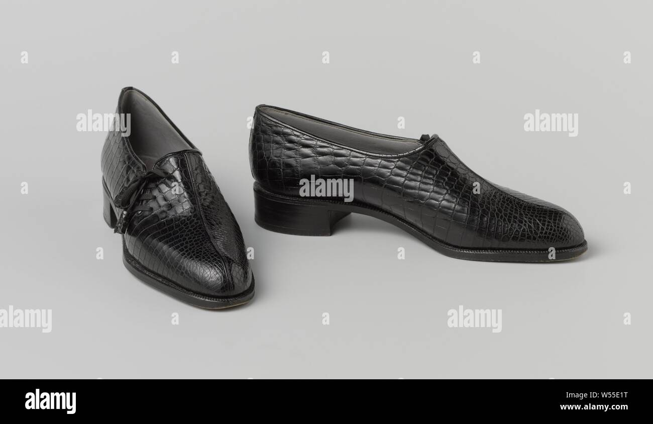 Pair of Lace-Up Shoes Slip-on black crocodile leather with asymmetrical lacing, Right slip-on of black crocodile leather with asymmetrical lacing wash. Model: A straight seam runs down the forefoot over the forefoot. Split on the outside of the front cover. Low straight heel. Fully lined with gray leather. Inner sole with golden print. Decoration: the slit in the right half of the cover is closed with a black fabric lace with black crocodile leather tassels. Address (on the insole): A. VAN GOETHEM 15 RUE DE NAMUR / PRES LA PLACE ROYALE BRUXELLES. Note: the left shoe is written with ink: 127592 Stock Photo