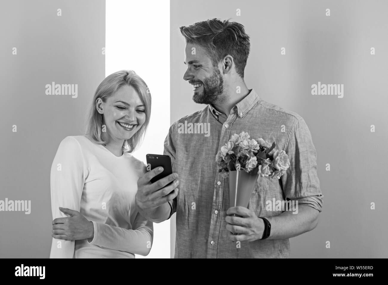Romantic concept. Couple in love interested by phone. Guy with phone and bouquet of flowers, pastel pink and green background. Man shows photo on smartphone to girl, sweet memories of their relations. Stock Photo