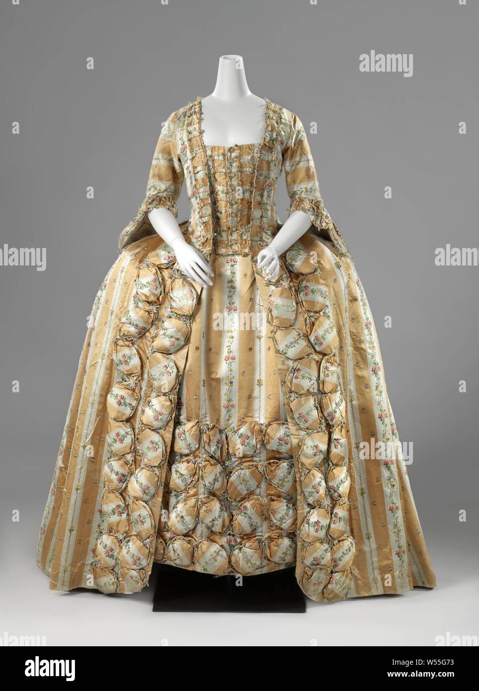 Silk frock or robe à la française with vertical yellow and white stripes and multi-colored bouquets with oval pouffes and lined with a multicolored ikat, frock or robe à la française made of silk with vertical yellow and white stripes and scatter motif multicolored bouquets, with oval pouffes and lined with a multicolored ikat. Model: Square neckline, half-length close-fitting sleeves with engaging and loose-fitting open skirt. The body closes in the front center with nine buttons. To this end, an additional strip of cover has been applied to the inner body of the striped cover, which is Stock Photo