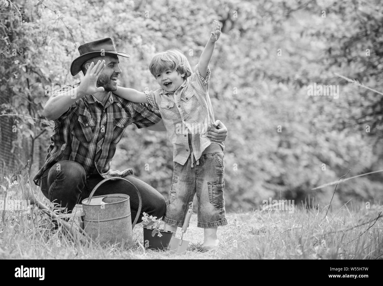 small boy child help father in farming. happy earth day. Family tree nursering. Eco farm. watering can, pot and hoe. Garden equipment. father and son in cowboy hat on ranch. Watering bed. Stock Photo