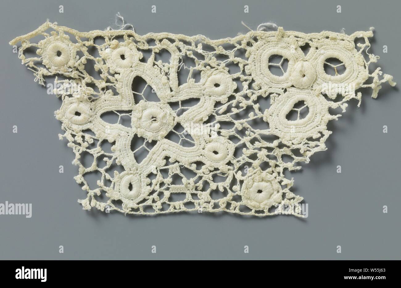 Strip crocheted lace with five-pointed stars and flowers made with open circles, Part of a strip of natural-colored Irish crocheted lace. The original, repeating pattern consists of a double row with a total of eight triangular floral patterns made with open circles, interspersed with one five-pointed star with a circle in the middle and a circle at each point. Crocheted irregular mesh with picots. Top and bottom are finished with a straight edge., anonymous, Ierland, c. 1890 - c. 1909, cotton (textile), l 8.5 cm × w 5.5 cm Stock Photo