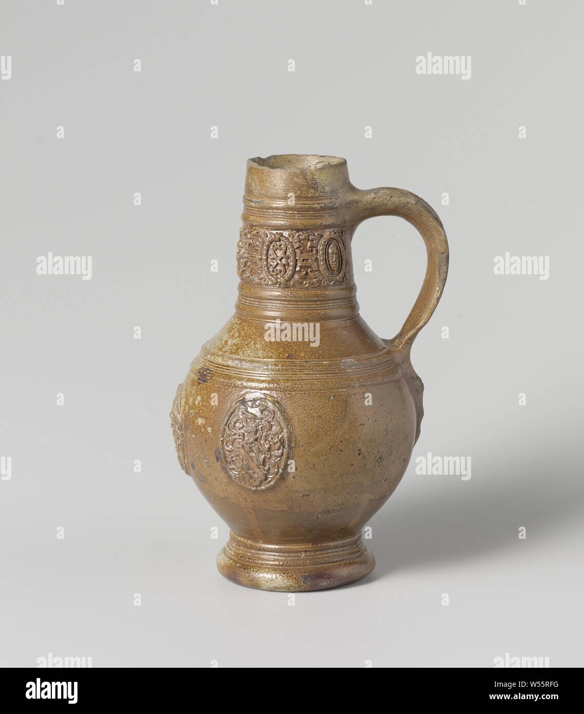 Jug with a coat of arms, Stoneware jug on high feet with a spherical body and long, narrow neck. The C-shaped ear is attached to the neck and shoulder. Profiles on the neck, shoulder and foot. Covered with a brown engobe. On the belly in relief three times a printed and imposed medallion with a weapon surrounded by aisles. On the neck a band of concatenated medallions with masks and surrounded by leaf vines. Raeren., anonymous, Raeren, c. 1550 - c. 1599, stoneware, glaze, engobe, vitrification, h 19.2 cm d 4.5 cm d 11.3 cm d 7.4 cm w 12.7 cm Stock Photo