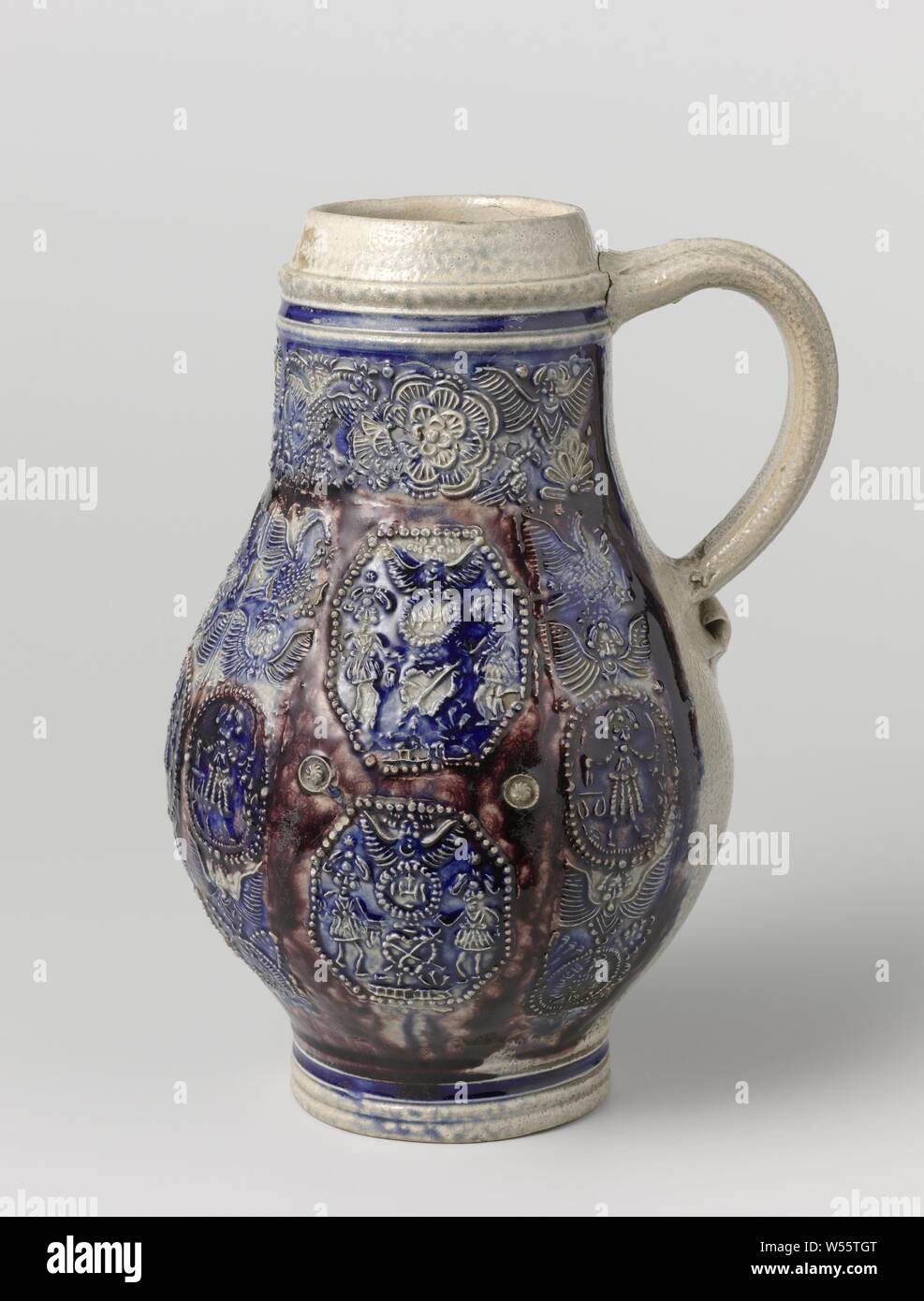 Jug with medallions, birds and flowers, Stoneware jug on stand ring with a pear-shaped body and wide neck. The C-shaped ear is attached to the neck and shoulder. Profiles on the neck and foot. Partially covered with cobalt blue and manganese purple. The front of the belly with various printed and imposed decorations embossed. Four times an octagonal medallion with the inscription 'IHS' surrounded by two men, an angel and a heart. These medallions are interspersed with five times a vertical band with angels, a bird and a medallion with Justitia. On the neck a horizontal band with angels Stock Photo
