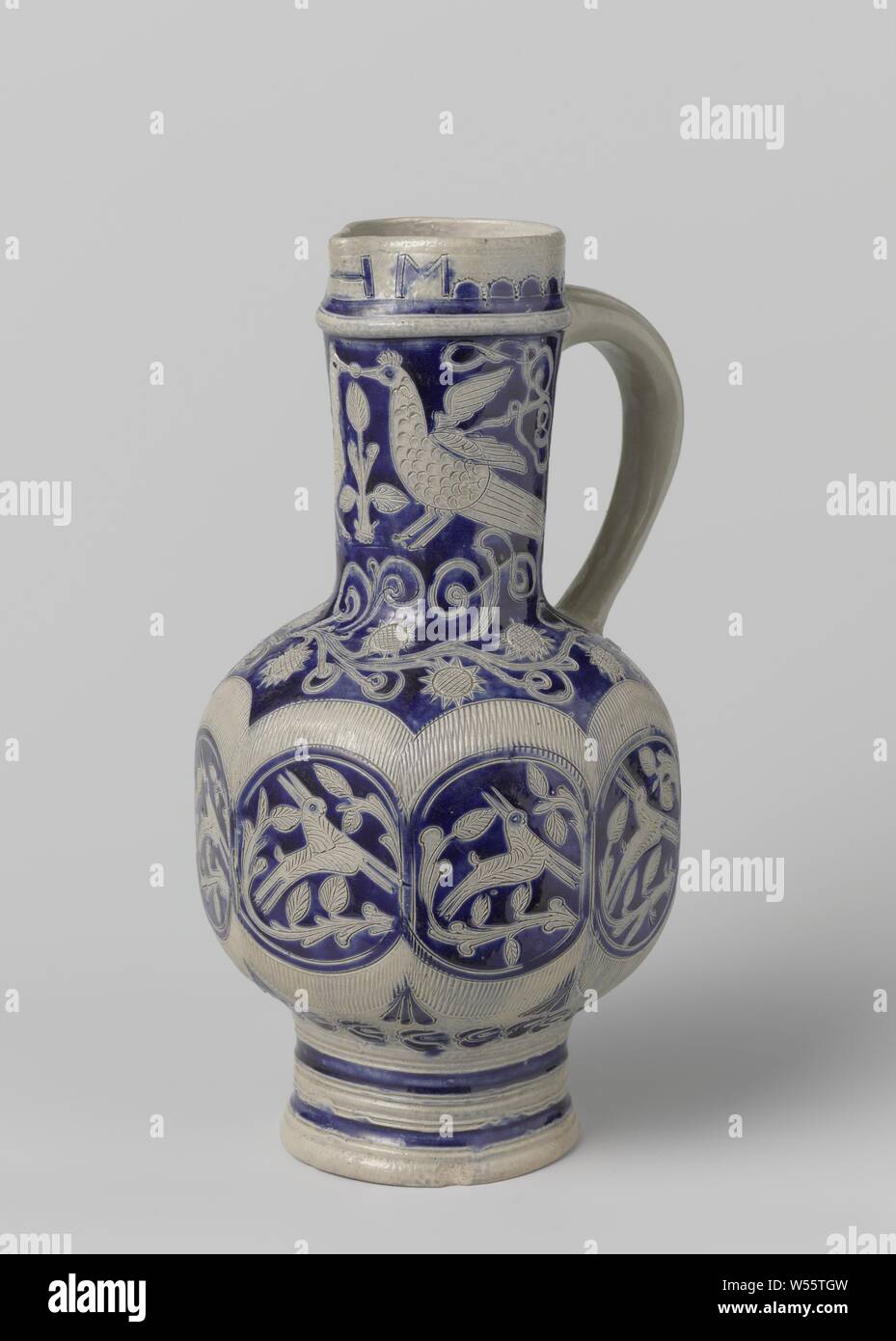 Jug with birds, hers and floral scrolls, Can of stoneware on high feet with a spherical, octagonal belly and long neck with a pinched spout. The C-shaped ear is attached to the neck and shoulder. Some profiles on the neck and foot. Partially covered with cobalt blue. On the belly eight medallions surrounded by a pressed zigzag line (knibis) and decorated with a hare between leaf vines. Two birds on the shoulder and neck between flower vines. Above the foot a band with stylized, stamped flowers. The incised letters 'HM' on the spout. Lahntal, Westerwald., anonymous, Lahntal, c. 1740 - c. 1760 Stock Photo