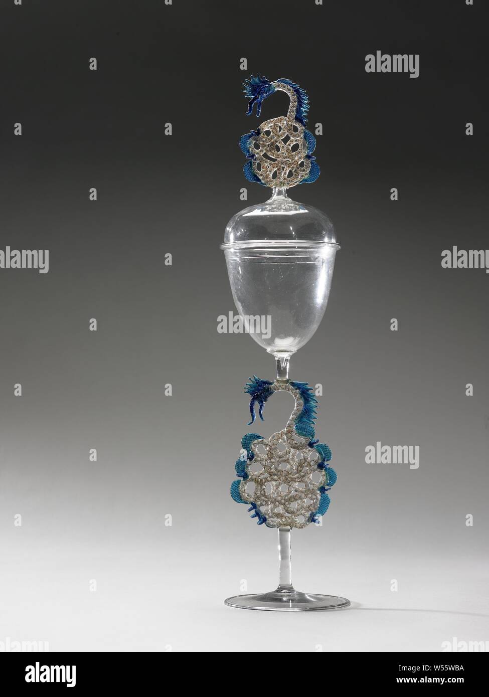 Goblet with lid, with winding snakes, Goblet on flat foot with folded edge. The trunk is made up of a straight bar of colorless glass, a middle part formed by a twisted tube with a yellow, white and blue spiral, in the form of a snake with blue wings and ending in a serpent head. Above a connecting piece a funnel-shaped cup, rounded at the bottom. Bulb lid, the bud constructed as the middle part of the trunk., C.H.F. Müller, Hamburg, c. 1865 - c. 1870, glass, glassblowing, h 46.0 cm × d 10.6 cm Stock Photo