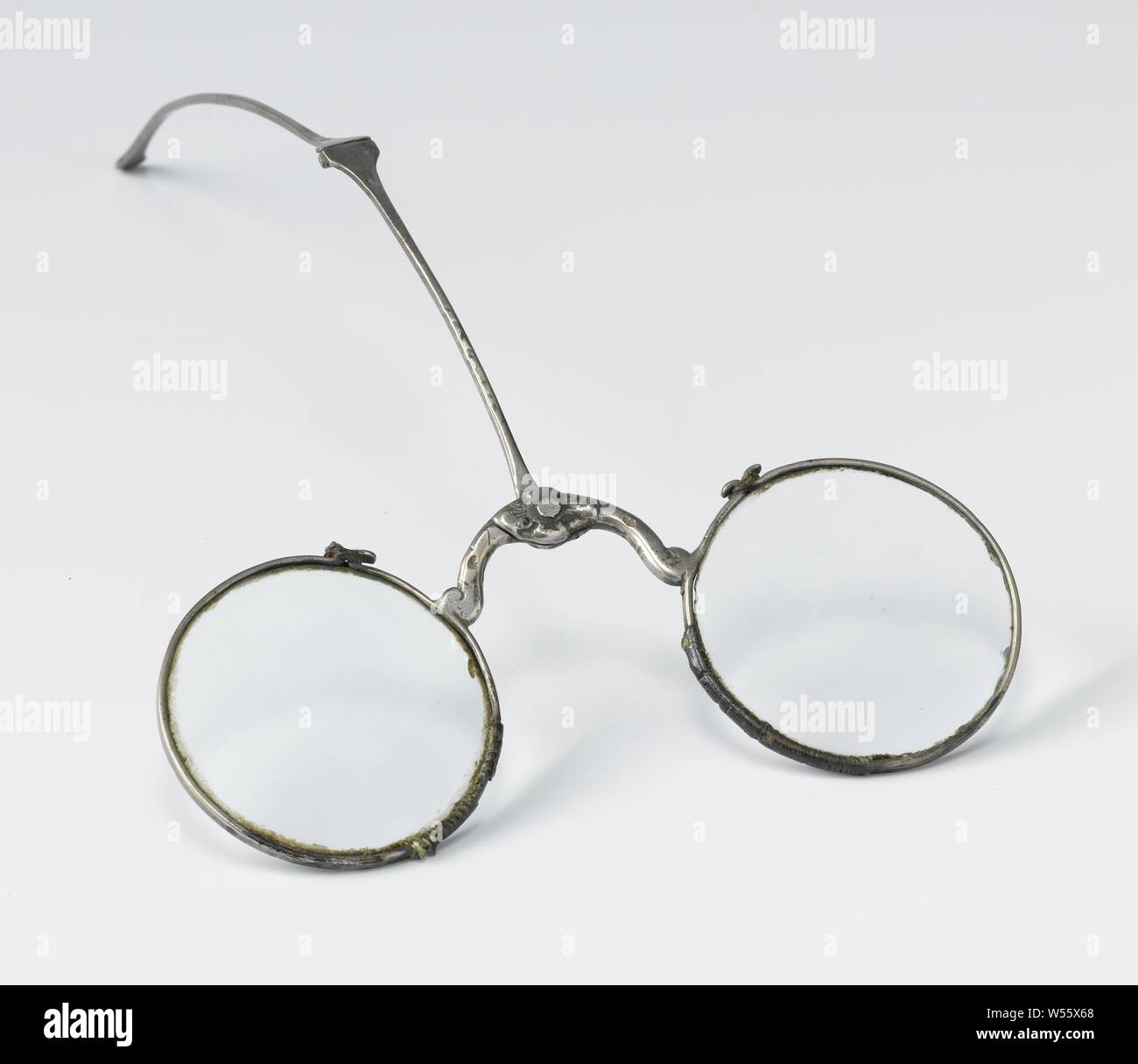 Forehead glasses with silver frame and polished round lenses, Forehead glasses with silver frame with spoon attached to the bridge between the lenses and ground round lenses. Model: In the middle of the arch-shaped bridge, ending in a curl on the rim around the glass, a pin is attached that fixes the spoon to the glasses. The spoon has a hinge halfway. The edges around the glasses are open at the top and bent back so that they form a hook with a metal wire around it for closing., anonymous, Netherlands (possibly), c. 1675 - c. 1775, montuur, glazen, grinding, l 9 cm d 3.5 cm Stock Photo