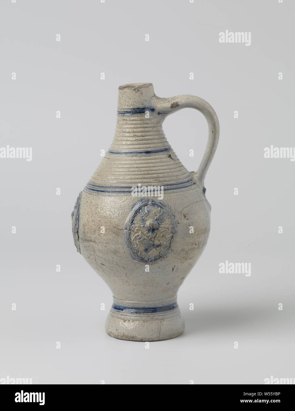 Jug with three coat of arms, Stoneware jug on high feet with an egg-shaped body and tapered neck. The C-shaped ear is attached to the neck and shoulder. A wide band of profiles on the neck and shoulder, some on the foot. Partially covered with cobalt blue. Three times a printed and imposed weapon on the abdomen with a cross on the shield, leaf vines and a winged helmet sign. Blue lines on the neck and foot. Westerwald., anonymous, Westerwald, c. 1600 - c. 1649, stoneware, glaze, cobalt (mineral), vitrification, h 20.2 cm d 2.7 cm d 11.1 cm d 6.5 cm w 11.7 cm Stock Photo