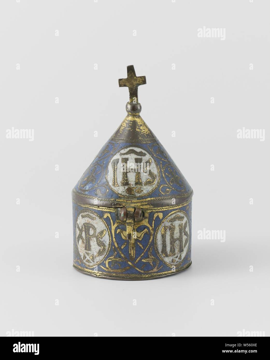 Pixis with medallions with the letters IHS and the monogram XPS, Pixis of gilt copper and enamel champlevé. The body is cylindrical. The conical lid is crowned by a cross on a sphere. The lid is connected to the body with a hinge and on the opposite side has a pierced snub which fits on the body between two eyes and can thus be closed with a pin. The lid is adorned with blue enamel ground, on which tendril ornament encloses four on the body, and on the lid three medallions of white enamel. The medallions show the letters IHS and the monogram XPS alternately. The bottom is connected to IHS (' Stock Photo