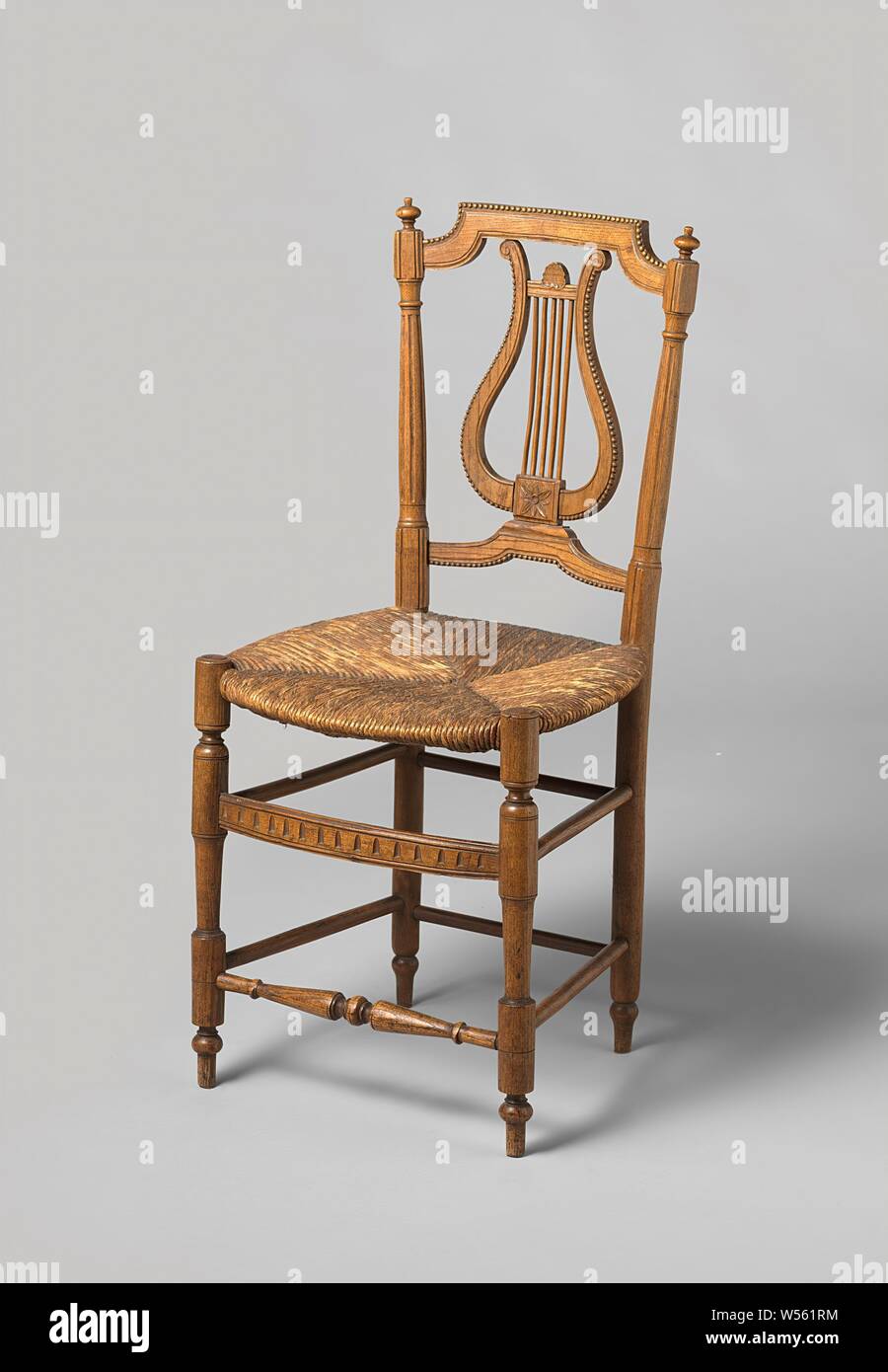 Chair with seat mat and fluted back posts crowned with buttons, Chair made of ash wood, seat made of matt straw. The hind legs are smooth, the front legs with turned houses with sections, connected by four sports below and above. The upper front apron is flat with a braided band, the under-fore has twisted sections. The open, hollowed back frame with fluted posts, crowned with buttons, has a straight upper sill with rounded corners and a cord-shaped sill, trimmed with pearl edges. In the middle a winch decorated with pearl edge and rosette., anonymous, Normandie (possibly), 1785 - 1800, wood Stock Photo