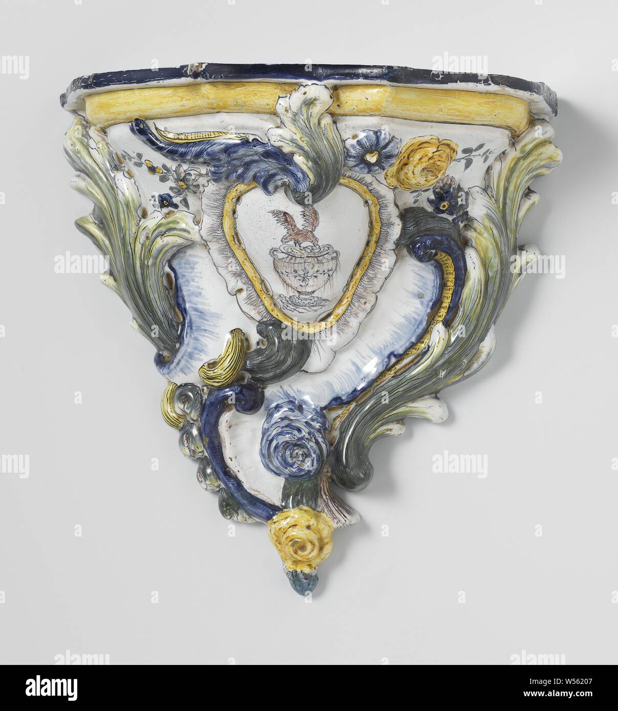 Console, multi-colored with bird picking fruit from a vase, Console with multi-colored faience. In a inverted pear-shaped medallion in relief a bird is painted that picks fruit from a vase. Leaves and flowers are modeled in relief around the medallion. The console is painted in the colors blue, green, yellow and purple., anonymous, West-Europa, c. 1775 - c. 1850, earthenware, tin glaze, h 29.0 cm × w 29.0 cm × d 16.0 cm Stock Photo