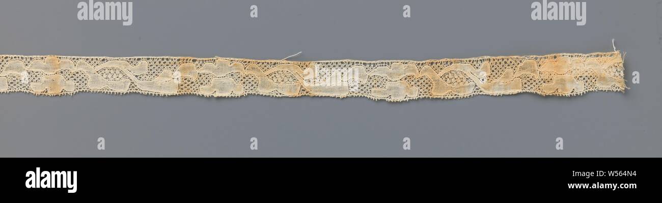 Strip of bobbin lace with double three-leaf flower, Strip of natural-colored bobbin lace, old-Flemish lace. The repeating and continuous pattern consists of a three-leaf flower mirrored along the longitudinal axis, alternated by two elongated leaves. The simply designed flowers are not entirely identical to each other, the upper flower has pointed petals. The motifs are connected by a lattice ground, a five-hole ground. The motifs are made in linen with contour threads. In a space between the elongated leaves, the partly bending over one another, a decorative ground is applied, a snow ground Stock Photo