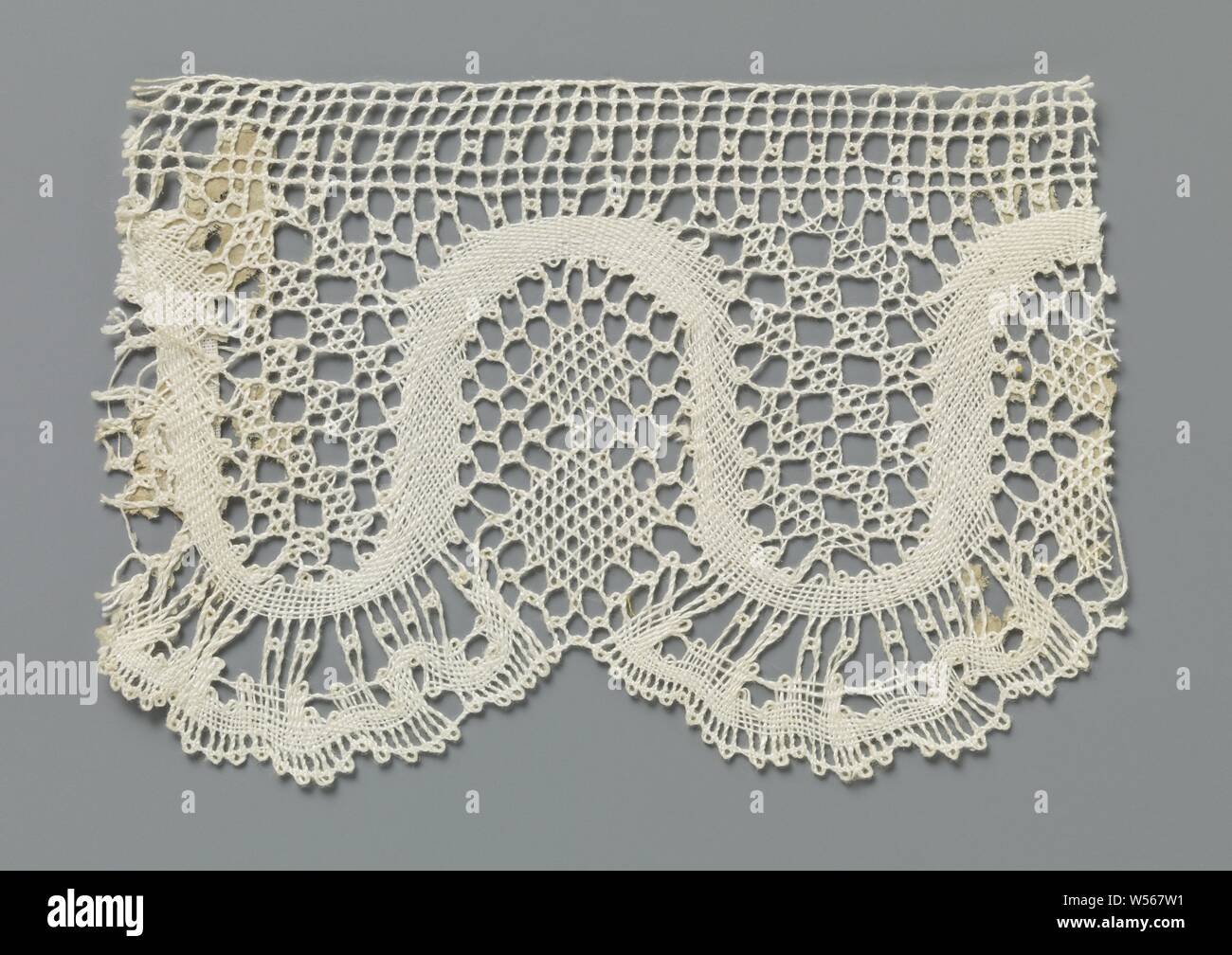 Strip of bobbin lace with a regular wavy line and fan scales, Strip of natural-colored bobbin lace: lace. The repeating pattern consists of a regularly wavy line in linen. The waves form u-shaped fields. Below the wave top there are two diamonds placed underneath each other in net stroke, the wave top touches the straight decorative band along the top of the strip. Fan-shaped shells hang under the wave valleys. In the golf valleys, an ornamental soil is used that forms square blocks. The top of the strip is finished straight., anonymous, Russia, c. 1900 - c. 1924, linen (material), torchon Stock Photo