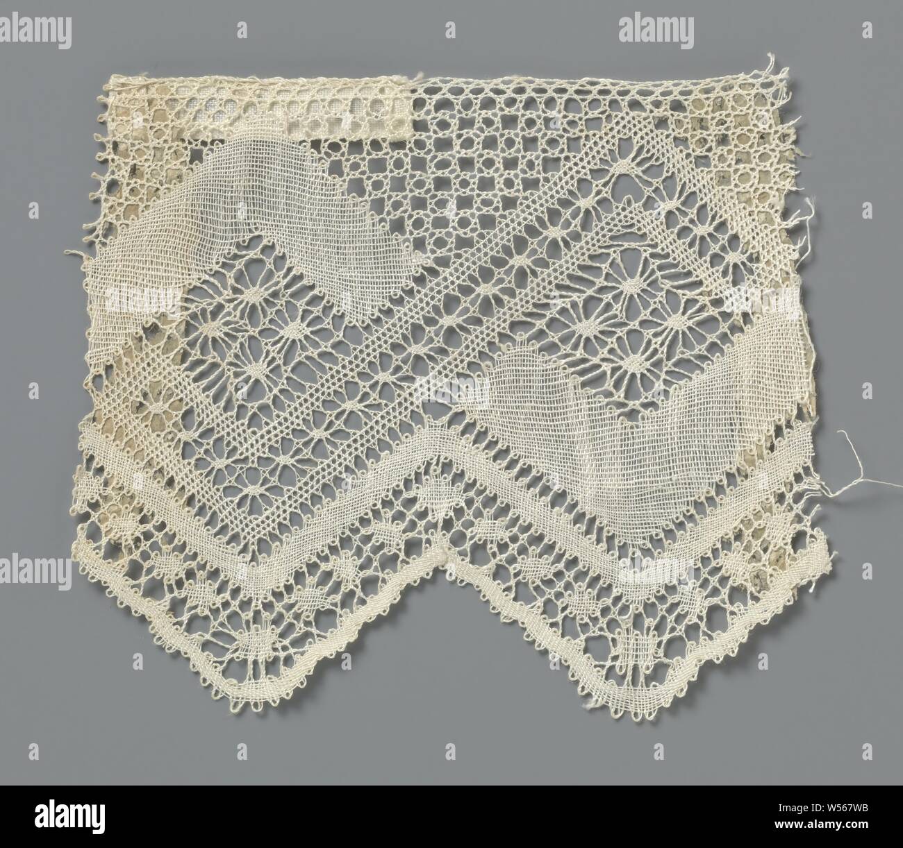 Strip of spool lace with diamonds between double zigzag band, Natural spool of lace strip, lace. The pattern consists of intersecting bands that cross the strip with a zigzag movement, creating diamonds and triangles. One band is made in densely worked linen stroke, the over-cutting decorative band is made in net stroke with snowflakes in between. Immediately below, two narrower and continuous zigzag webs with larger snowflakes in between form the triangular scallops along the underside of the strip. The zigzag webs are connected to each other along the top of the strip by a mesh ground. Stock Photo