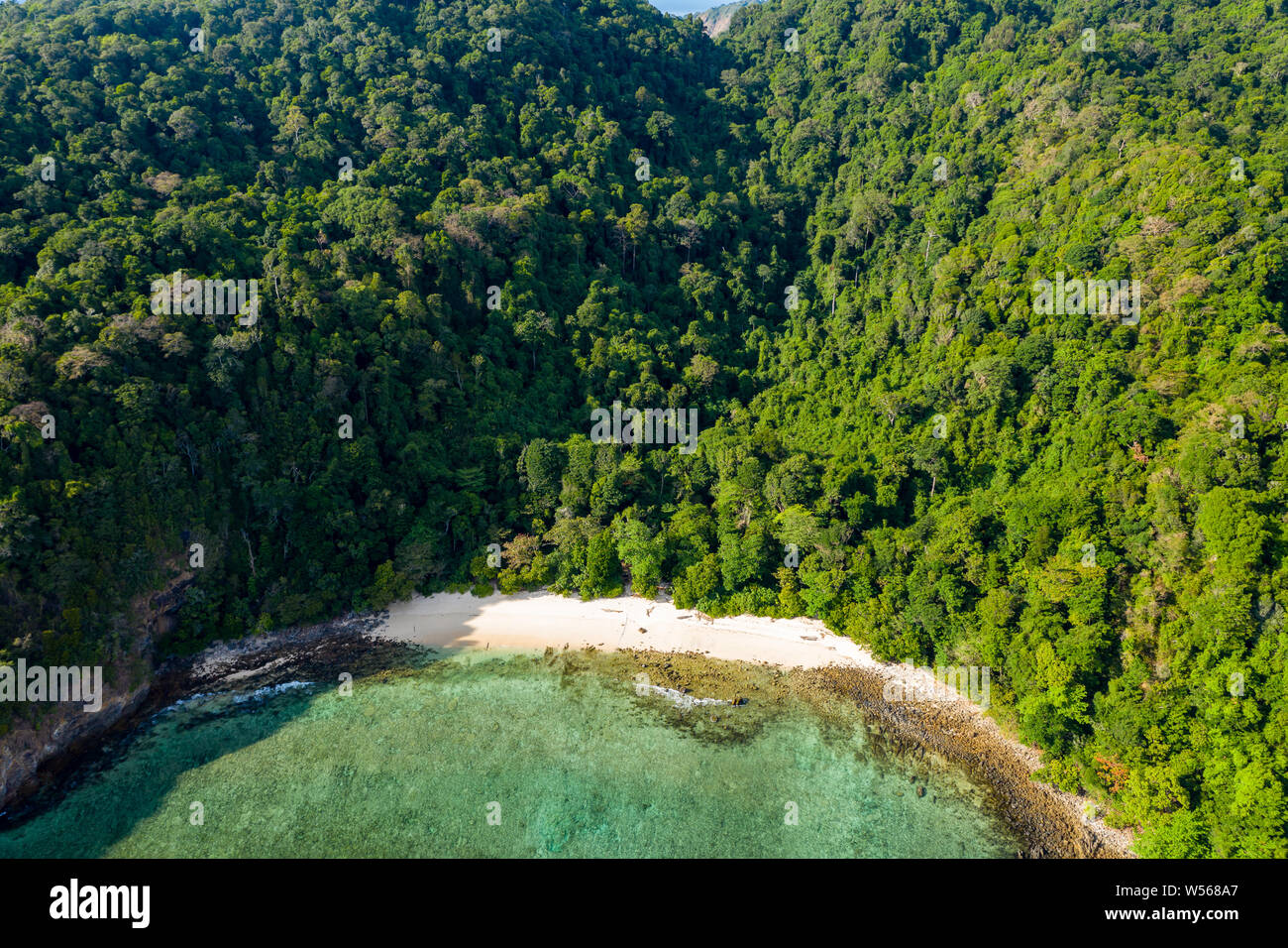 Aerial drone view of a small beach on a lush, green tropical island Stock Photo