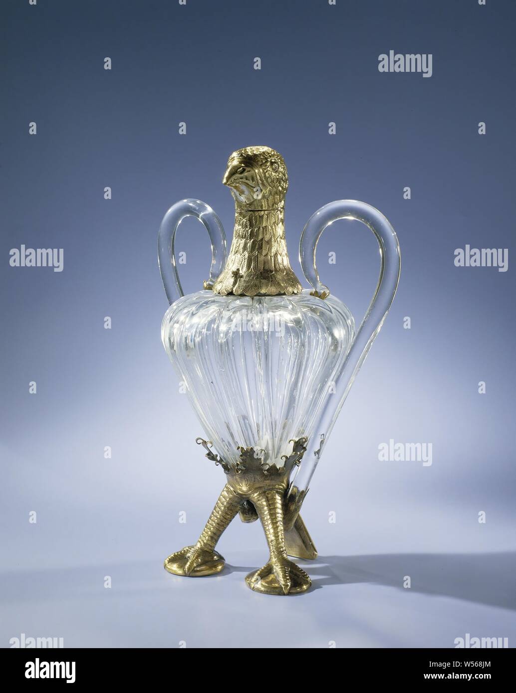 Eagle-shaped carafe, Vase-shaped body with thick ribs, mounted in the shape of an eagle, with two legs, a tail and an eagle's head of gilt silver. The removable head acts as a stop. Tail, neck and head are engraved with scales, the tail, neck and head with feathers., anonymous, Germany (possibly), c. 1800 - before 1875, glass, montuur, engraving, h 26.9 cm × w 18.0 cm × d 12.3 cm Stock Photo