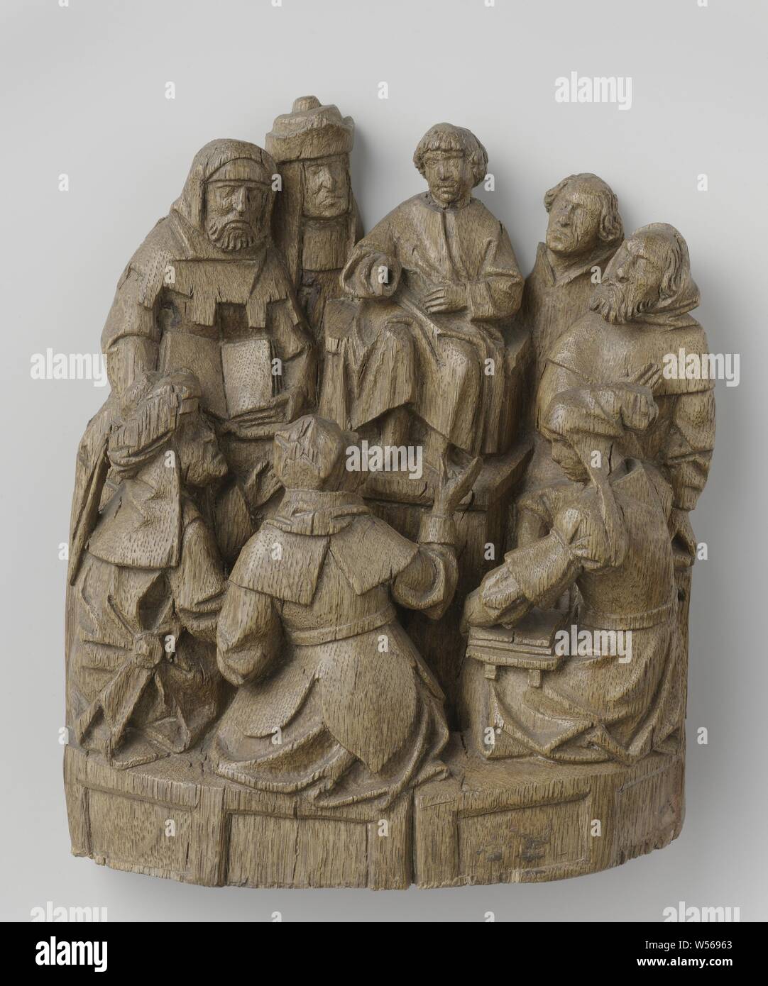 Jesus among the scribes, Jesus, as a boy, sits on a platform surrounded by listeners. Two people on each side and three people on a slightly lower bench opposite him. Jesus holds the left hand in front of the waist and the right arm bent and slightly forward. A few listeners gesture with their hands, two others hold an open book on their lap. Christ wears a tunic, the Pharisees are dressed in various robes and with a cap, turban or hat. The bnk, on which the three front seats are seated, has sunken panels. The hooded man, on the far right, may represent Joseph, Christ's dispute with Stock Photo