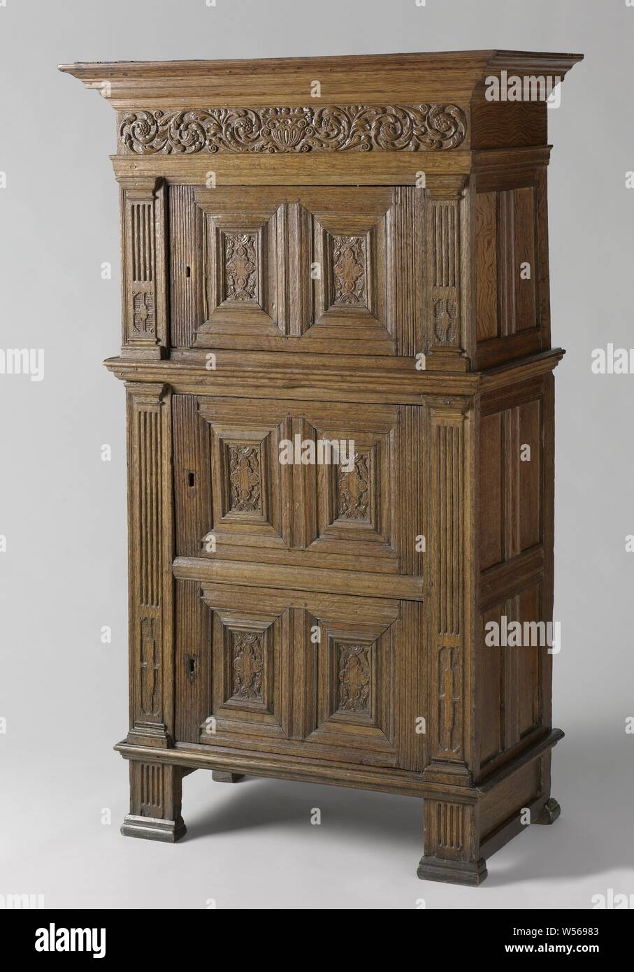 Oak cabinet with one-door upper cabinet and two-door lower cabinet, Oak cabinet, consisting of a one-door upper cabinet and a two-door lower cabinet. The corner posts bear Tuscan pilasters. The panels of the doors are decorated with a chain ornament and acanthus leaf within profiled frames. The main frame has a stabbed frieze with a fruit bowl, flanked by acanthus vines. The panels of the sides are unadorned., anonymous, Noord-Holland, c. 1600 - c. 1650, wood (plant material), oak (wood), h 172.5 cm × w 101 cm × d 55.5 cm Stock Photo