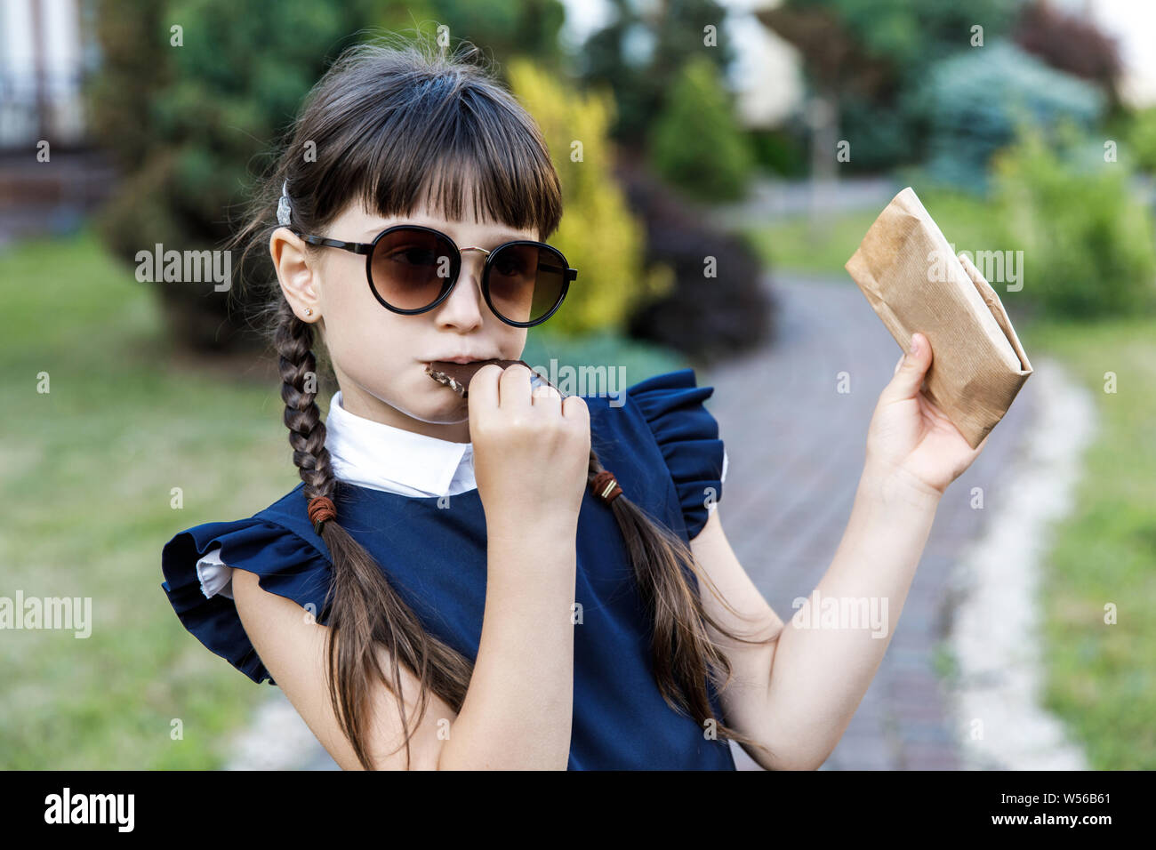 Cute girl, school years dressed in school uniform with pleasure eating black chocolate on the street Stock Photo