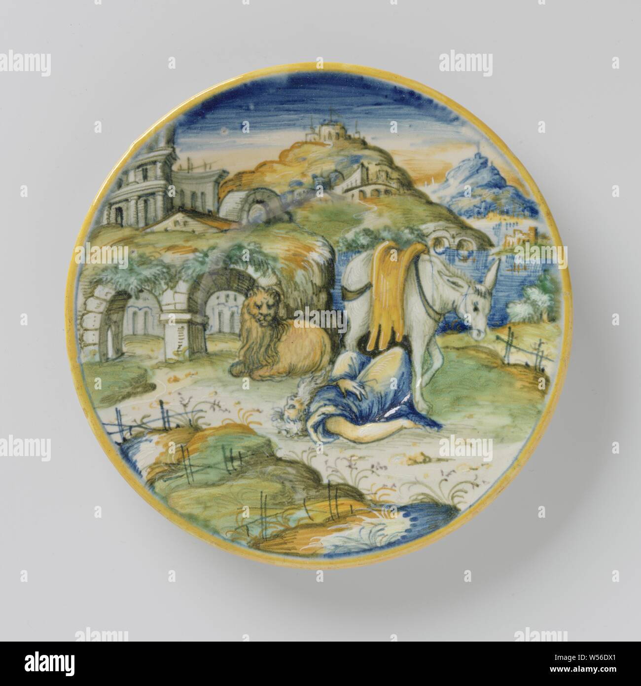 Plate with the disobedient prophet, Round plate of multi-colored majolica. The story of the disobedient prophet is painted on the board (I Kings 13). In a mountain landscape a man (the disobedient prophet) is lying on the ground, behind him is a donkey and a lion. On the back of the board is a text painted (manda il verbo ...), the body of the prophet or Judah groin intact on the road with the donkey and the lion beside it, anonymous, Venice, c. 1570 - c. 1580, earthenware, tin glaze, lead glaze, d 22.0 cm × h 2.4 cm Stock Photo