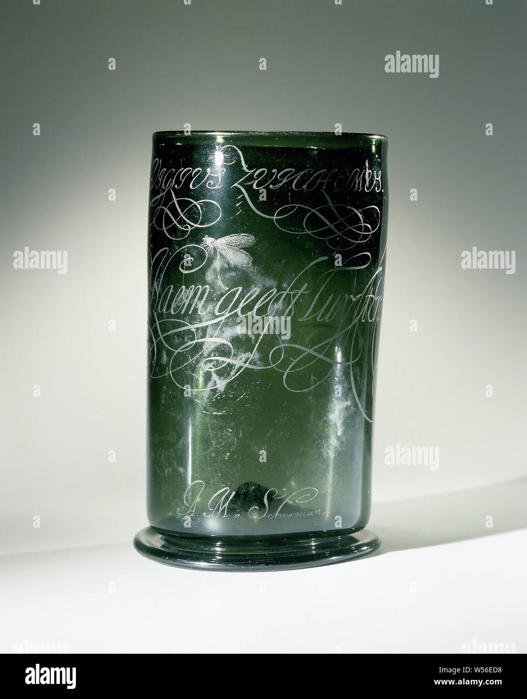 Cup with the inscription: Al schyn ick duyster De Naem gives luyster, Cup of dark green glass. Inserted soul. Smooth, hollow stand ring. On the high cylindrical body the calligraphic inscription: 'VIGLIUS ZUICHEMUS' and 'Al schyn ick duyster, De Naem gives luyster' (on the 'N' of 'Naem' a dragonfly or fly). Above the stand ring the signature 'A.M. à Schurman ', Viglius Zuichemus Ab Aytta, anonymous, c. 1500 - c. 1600 and/or c. 1630 - c. 1670, glass, glassblowing, h 20.5 cm × w 12.7 cm × d 12.5 cm d 12.3 cm Stock Photo