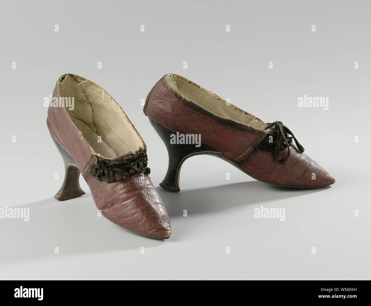 Pair of Ruched Women's Shoes Dark red leather shoe adorned with two rows of black silk ruffles on the forefoot cut, Dark red leather shoe. Model: The nose is pointed, one front and two side blades. The stitching that holds the sheets together was originally covered with black silk bands. The front of the heel runs straight down in a rounded corner from the geleng. The side and back of the narrow heel are fitted and covered with black leather. Along the edge of the heel are white stitching. Leather back and roughened leather sole. Side sheets and front sheet are lined with beige linen. A Stock Photo