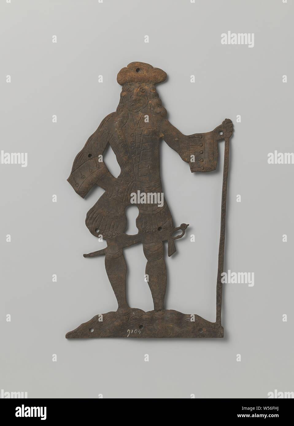 Key plate in the shape of a man, Key plate of iron in the shape of a man. The man with long, loose hair wears a headdress. His jacket has wide cuffs and a double row of buttons on his lapel. Underneath he wears shorts and shoes with a small heel. He holds a stick in his left hand. A sword or saber can be seen behind his knees. The opening of the keyhole is arranged between the upper legs., anonymous, West-Europa, 1675 - 1725, iron (metal), engraving, h 23.9 cm × w 13.7 cm Stock Photo